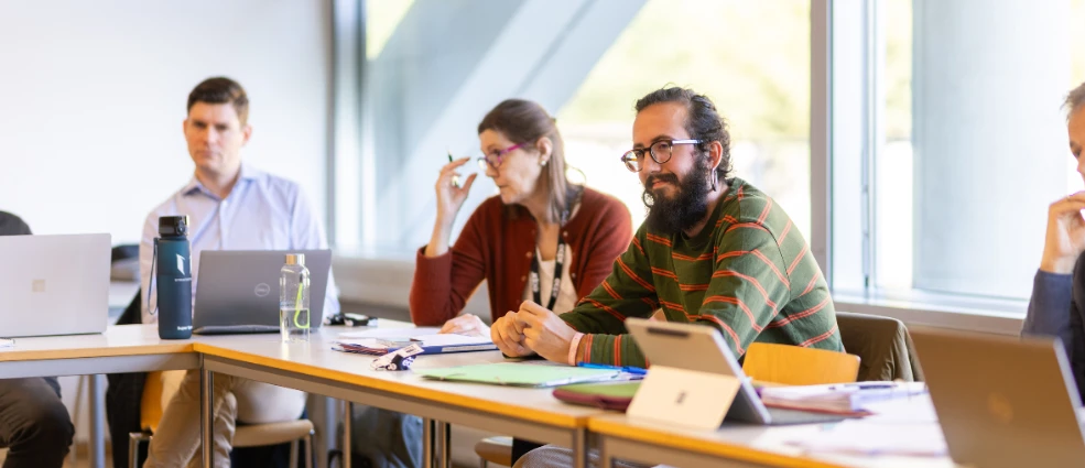 People seated a meeting room with laptops and papers on the table during an ECPR Workshop in Innsbruck. A man in a striped jumper is in the foreground.