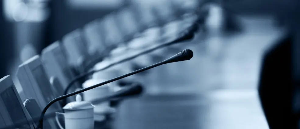 A conference table with gooseneck microphones and chairs around it